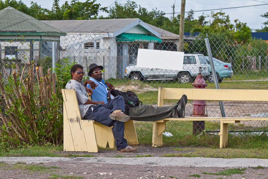 Два чёрных мужчины-пассажира в тёмных очках ожидают рейса на жёлтых скамейках. Аэропорт Барбуда Кодрингтон, остров Барбуда, Антигуа и Барбуда. Two black male passengers in dark glasses are waiting for a flight on yellow benches. Barbuda Codrington Airport (IATA: BBQ), Barbuda island, Antigua and Barbuda, Caribbean.