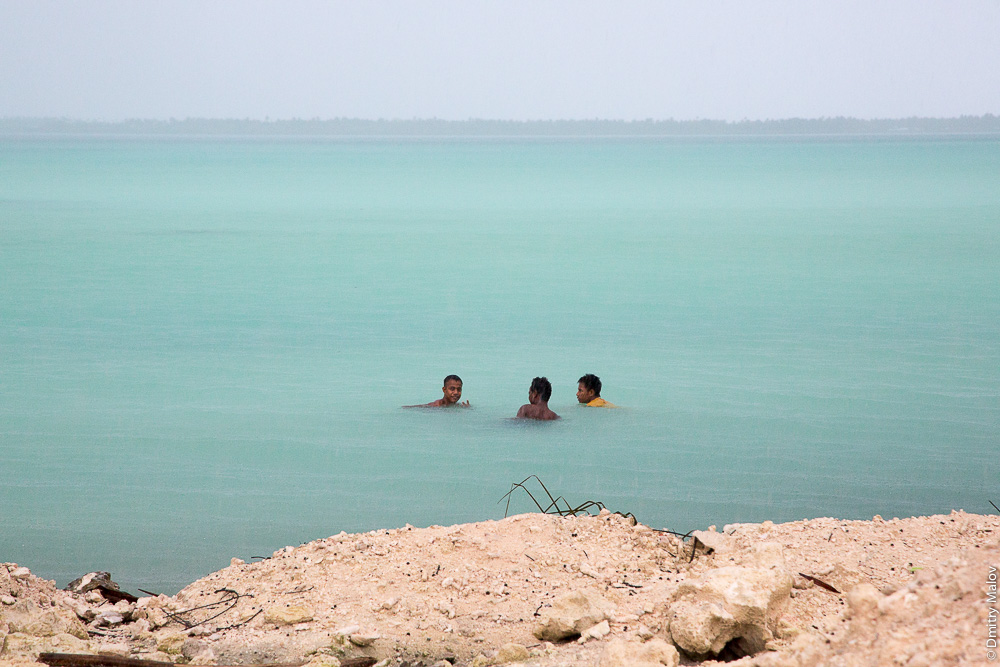 Три местных мужчины купаются под дождём в лагуне атолла Тарава, Кирибати, Микронезия. Three local men swimming in the rain in the lagoon of Tarawa atoll, Kiribati, Micronesia.