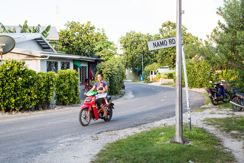 Namo road sign. Деревня Ваиаку, атолл Фунафути, Тувалу. Vaiaku village, Fongafale island, Funafuti atoll, Tuvalu. A local Polynesian woman with a kid on a bike. Местная жительница с ребёнком на мотоцикле.