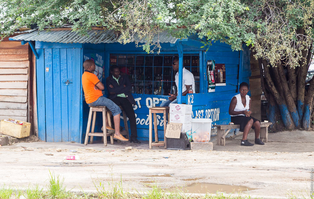 Black people near a shop on streets of Sesheke town, Zambia, Africa. Чёрные африканцы у кафе-магазина на улице города Сешеке, Замбия, Африка.