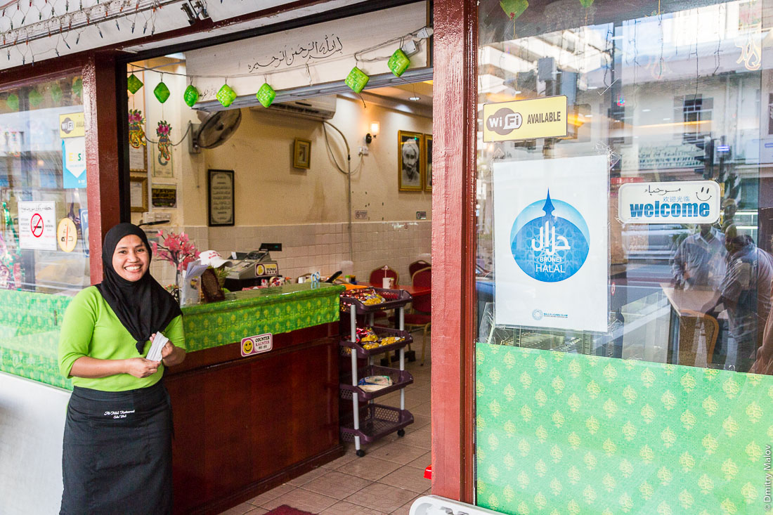 Хозяйка кафе в бурке — традиционной мусульманской одежде, Бандар-Сери-Бегаван, Бруней-Даруссалам. Lady in burka welcomes guests to a cafe. Brunei Halal logo. Bandar Seri Begawan, Negara Brunei Darussalam.