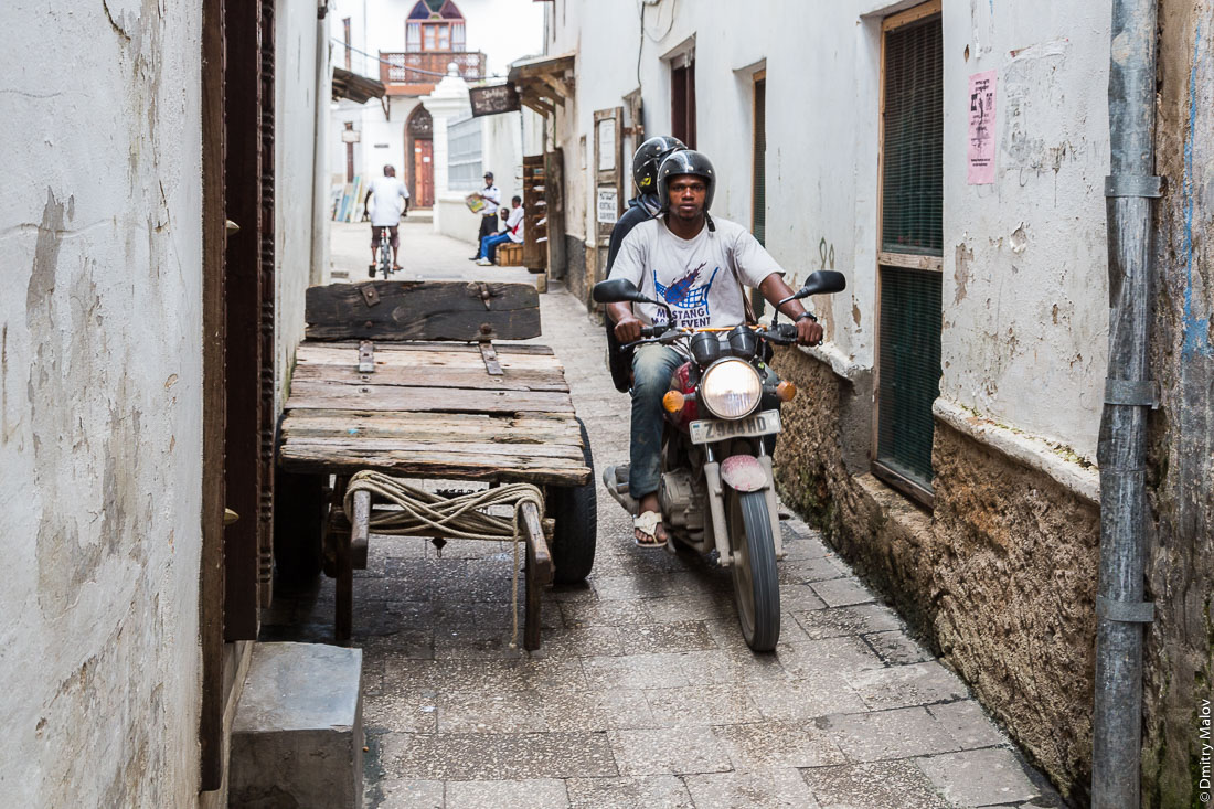Мотоциклисты на пешеходных улицах. Каменный город, старая часть Занзибар-сити, остров Унгуджа, Танзания. Local Motorcyclists on pedestrian streets. Stone Town, old town of Zanzibar City, Unguja island, Tanzania