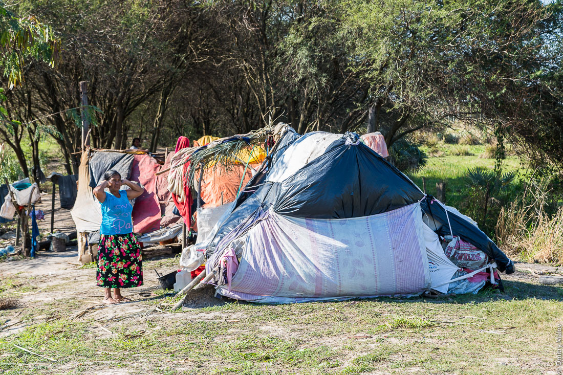 Пожилая индейская женщина стоит на фоне палатки, трущобы вдоль дороги№9 Рута Трансчако, Гран-Чако, Парагвай. An elderly native american woman stands with a tent in the background, slums along the road number 9 Ruta Transchaco, Gran Chaco, Paraguay.