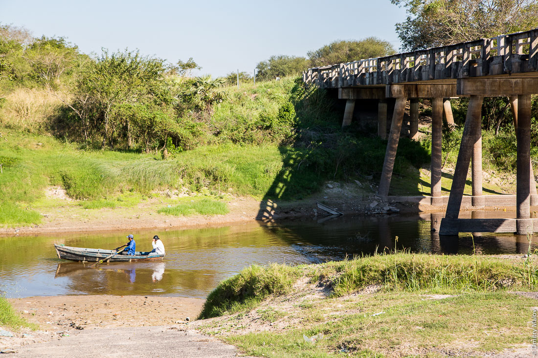 Два человека гребут на лодке под мостом дороги №9 Рута Трансчако, Гран-Чако, Парагвай. Two people on a rowing boat under the bridge of the road number 9 Ruta Transchaco, Gran Chaco, Paraguay.