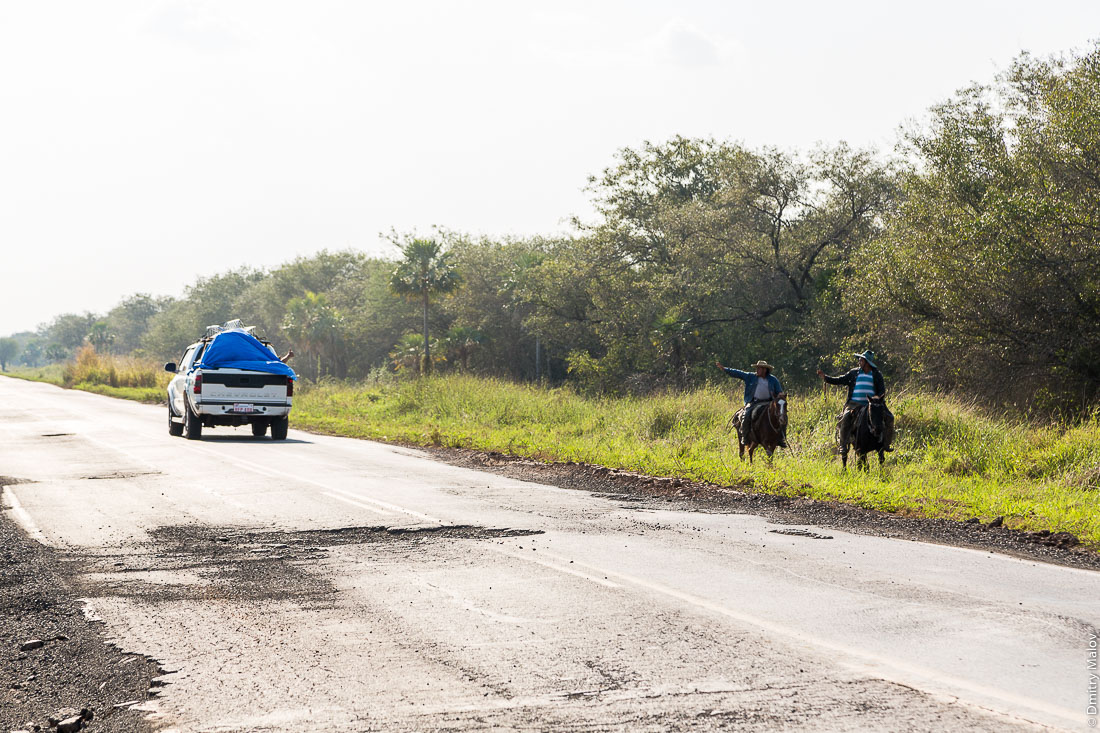 Два индейца на лошадях приветствуют проезжающую машину у дороги№9 Рута Трансчако, Гран-Чако, Парагвай. Two Native Americans on horses are hailing a passing car on the road number 9 Ruta Transchaco, Gran Chaco, Paraguay.