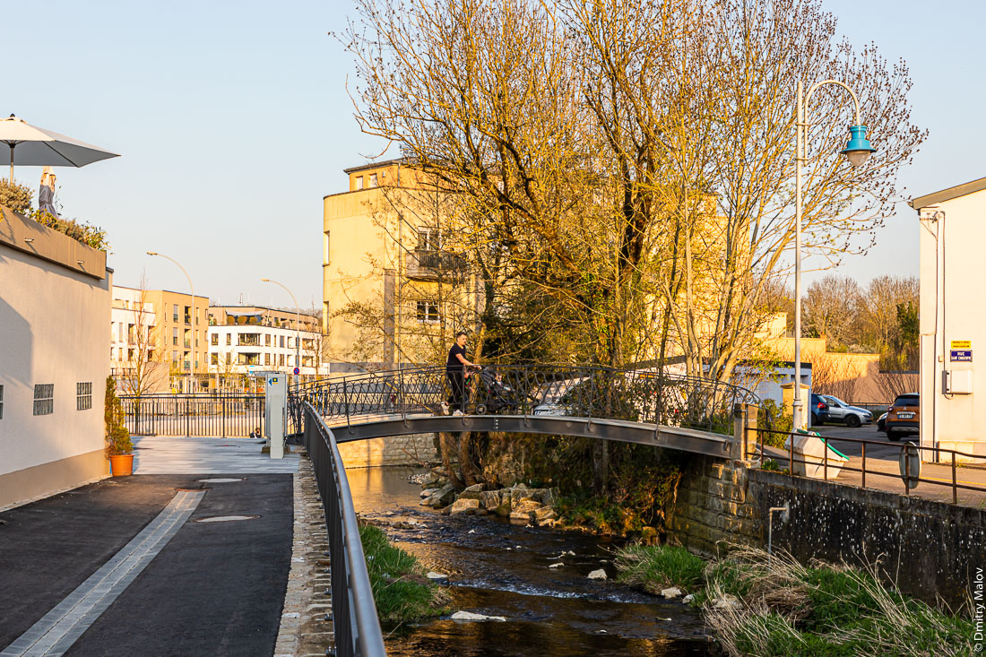 A man with a kids pram crosses Gander river in Mondorf-les-Bains, Luxembourg. Мужчина с детской коляской пересекает реку Гандер в Мондорф-ле-Бен, Люксембург. Люксембургско-французская граница в центре города Мондорф-ле-Бен, Люксембург и Мондорф, Франция. Река Гандер