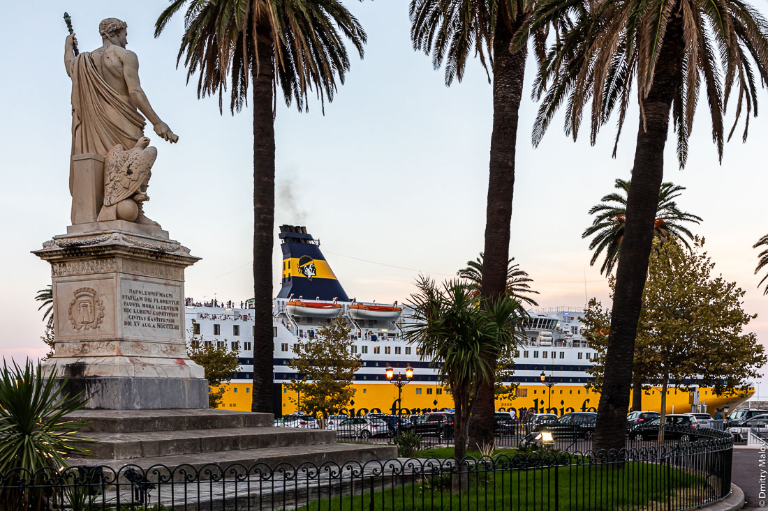 Желто-синий паром Corsica Ferries - Sardinia Ferries c логотипом в виде корсиканского национального символа головы мавра выглядывает из-за пальм в Бастии, Корсика. Статуя Наполеона