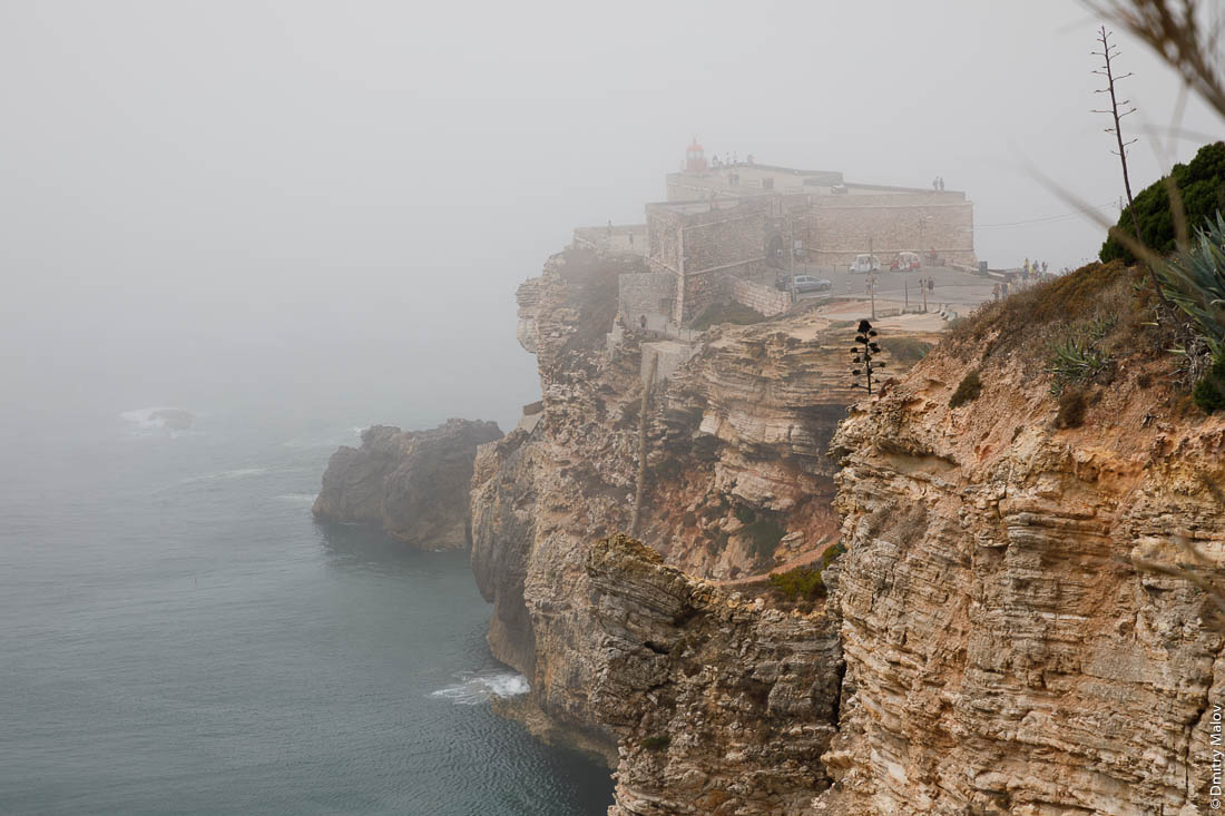 Форт Сан-Мигель-Арканжу на мысу в тумане на фоне спокойного моря, Назаре, Португалия. Fort of São Miguel Arcanjo