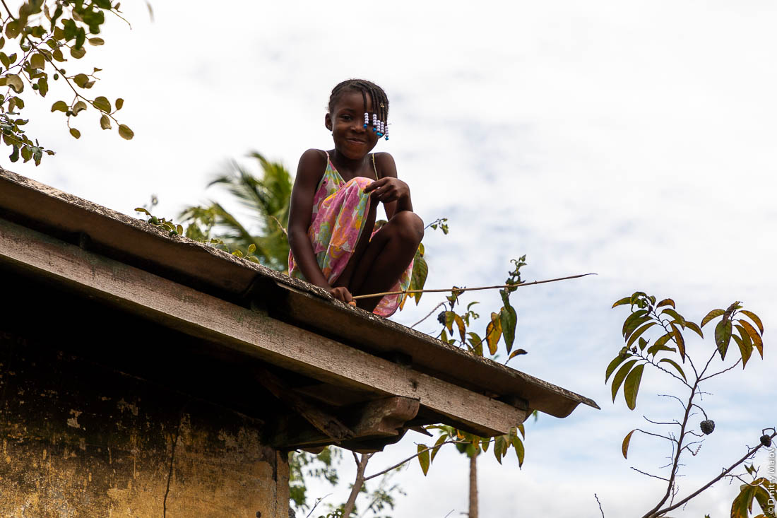 Маленькая чёрная африканская девочка сидит на крыше, остров Сан-Томе, Сан-Томе и Принсипи
