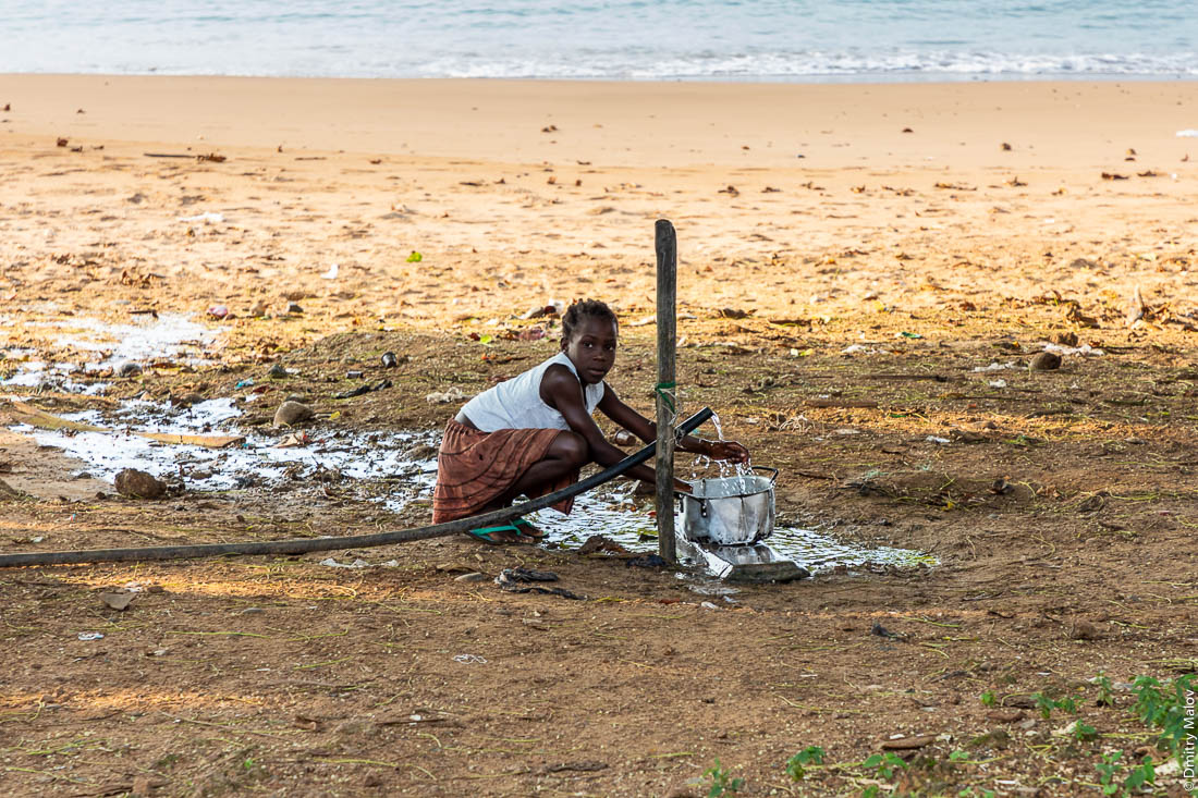Маленькая черная девочка моет посуду на пляже Praia Burra, остров Принсипи, Сан-Томе и Принсипи, Африка